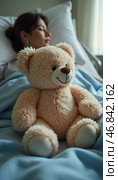 In a quiet hospital room, a gentle teddy bear sits close to a tired woman recovering from illness, symbolizing hope and comfort amidst her struggles. Soft light fills the space, enhancing the warmth. Стоковое AI-изображение, AI-художник Юлия Петровская / Фотобанк Лори