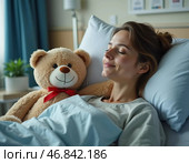 In a hospital room, a woman rests with a teddy bear by her side, symbolizing comfort and hope amidst her recovery journey. The warm ambiance offers solace during her hardship. Стоковое AI-изображение, AI-художник Юлия Петровская / Фотобанк Лори
