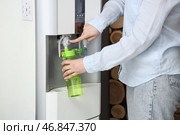 Женщина наполняет зеленую бутылку фильтрованной водой из кулера в комнате. Стоковое фото, фотограф Pixel_shot / Фотобанк Лори