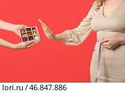 Молодая женщина с измерительной лентой отказывается от рук, держащих сладкие шоколадные конфеты на красном фоне. Стоковое фото, фотограф Pixel_shot / Фотобанк Лори