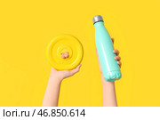 Женские руки с гантельным наклоном и бутылкой воды на желтом фоне, крупным планом. Стоковое фото, фотограф Pixel_shot / Фотобанк Лори