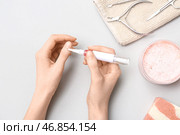 Женские руки наносят масло для кутикулы с ручкой, косметикой и маникюрными инструментами на сером фоне. Стоковое фото, фотограф Pixel_shot / Фотобанк Лори
