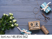 Календарь-куб с датой 8 МАРТА, подарочными коробками, белыми розами и ножницами на голубом деревянном фоне. Празднование Международного женского дня. Вид сверху. Стоковое фото, фотограф Pixel_shot / Фотобанк Лори