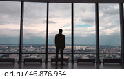 Rear view of man in formal suites who stand in front of panoramic window with city view. Стоковое фото, фотограф David Kashakhi / Фотобанк Лори
