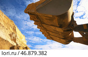 Bottom view of excavator bucket of yellow color loaded with sand on blue cloudy sky background. Стоковое фото, фотограф David Kashakhi / Фотобанк Лори