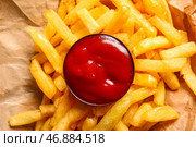 Вкусные картофельные ломтики и миска кетчупа на бумажке для выпечки, крупный план. Стоковое фото, фотограф Pixel_shot / Фотобанк Лори