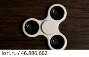 Spinning in motion of a popular white toy spinner on a wooden table. Стоковое фото, фотограф David Kashakhi / Фотобанк Лори