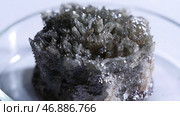Crystalline piece of dark untreated mineral lying on glass cup on white background. Стоковое фото, фотограф David Kashakhi / Фотобанк Лори