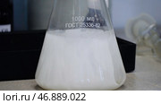 Laboratory glass Erlenmeyer conical flask filled with chemical white liquid for a chemistry experiment in a science research lab. Стоковое фото, фотограф David Kashakhi / Фотобанк Лори