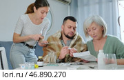 Portrait of focused elderly woman sitting at table reading instruction choosing medicines for her sick adult son, while her daughter-in-law trying to help and giving drugs to him. Стоковое видео, видеограф Яков Филимонов / Фотобанк Лори