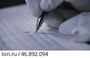 Close up of hands in white gloves writing data in the notebook with a pen on black background. Стоковое фото, фотограф David Kashakhi / Фотобанк Лори