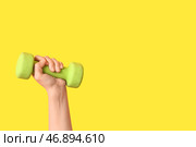Женская рука с зеленым гантелем на желтом фоне, крупным планом. Стоковое фото, фотограф Pixel_shot / Фотобанк Лори