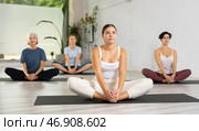 Concentrated young woman performing Butterfly Pose Baddha Konasana during yoga class with female group. Стоковое фото, фотограф Яков Филимонов / Фотобанк Лори