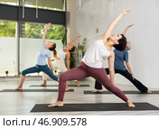 Young Latin female practicing Revolved Side Angle Pose Parivrtta Parsvakonasana, balancing posture of Hatha yoga during group workout in studio. Стоковое фото, фотограф Яков Филимонов / Фотобанк Лори