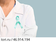 Взрослая женщина-врач с бирюзовой лентой на синем фоне, крупный план. Месяц осведомленности о здоровье шейки матки. Стоковое фото, фотограф Pixel_shot / Фотобанк Лори
