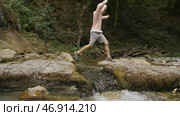 Side view of a boy jumping over the mountainous water stream. Стоковое фото, фотограф David Kashakhi / Фотобанк Лори