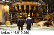 Back view of metallurgists walking inside the hot shop of the metallurgical production plant. Стоковое фото, фотограф David Kashakhi / Фотобанк Лори