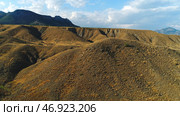 Close-up view of sand and gravel hills and ravines near the mountains covered with green shrubs and trees against blue sky. Стоковое фото, фотограф David Kashakhi / Фотобанк Лори