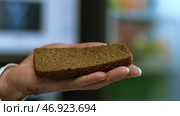 Close-up of man's hand holding a piece of Borodino rye bread with slice of Doctor's sausage falling on it. Стоковое фото, фотограф David Kashakhi / Фотобанк Лори