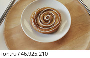 Tasty sweet puff rolls with honey and white glaze lying on the white plate and rotating on the wooden round board. Стоковое фото, фотограф David Kashakhi / Фотобанк Лори