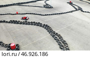 Aerial view of kart racers in protective uniform and helmet moving on the track with old black car tires in the city in sunny day. Стоковое фото, фотограф David Kashakhi / Фотобанк Лори