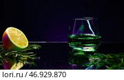 Close up of green alcoholic cocktail standing on a bar counter with orange and rosemary on a purple wall background. Стоковое фото, фотограф David Kashakhi / Фотобанк Лори