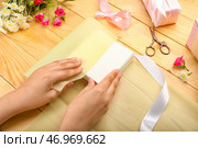 Женщина заворачивает подарочную коробку в бумагу на деревянном фоне. Стоковое фото, фотограф Pixel_shot / Фотобанк Лори