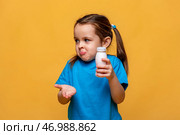 Puzzled and clueless little girl with arms out, shrugging her shoulders, holding bottle with yogurt, saying: who cares, so what, I don't know. Human emotions, facial expressions, yellow background. Стоковое фото, фотограф Ирина Михайличенко / Фотобанк Лори