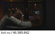Young woman sits on window and looks sadly at night city. Стоковое фото, фотограф David Kashakhi / Фотобанк Лори
