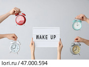 Руки, держащие различные будильники, и доска с надписью ВСТАВАЙ на сером фоне. Стоковое фото, фотограф Pixel_shot / Фотобанк Лори