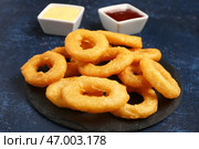 Черная доска с жареными панированными луковыми кольцами и различными соусами на голубом фоне. Стоковое фото, фотограф Pixel_shot / Фотобанк Лори