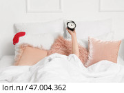 Женщина с будильником лежит под одеялом в спальне. Стоковое фото, фотограф Pixel_shot / Фотобанк Лори