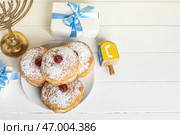 Тарелка с вкусными пончиками, подарками и крутящимся вертящимся для празднования Хануки на светлом деревянном фоне. Стоковое фото, фотограф Pixel_shot / Фотобанк Лори