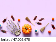 Хэллоуинская композиция с конфетными насекомыми, тыквами, скелетной рукой и метлами на лиловом фоне. Стоковое фото, фотограф Pixel_shot / Фотобанк Лори