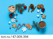 Рамка из вкусных печенья, какао с зефирками, карамельными палочками, хвоями, корицей, рождественскими шариками и снежинками на голубом фоне. Стоковое фото, фотограф Pixel_shot / Фотобанк Лори