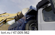 Excavator flipping the bucket of yellow color loaded with sand, loading the truck with sand (2022 год). Редакционное фото, фотограф David Kashakhi / Фотобанк Лори