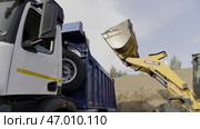 Excavator flipping the bucket of yellow color loaded with sand, loading the truck with sand (2022 год). Редакционное фото, фотограф David Kashakhi / Фотобанк Лори