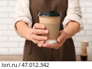 Молодая девушка-бариста с одноразовым стаканом кофе возле белой кирпичной стены. Стоковое фото, фотограф Pixel_shot / Фотобанк Лори