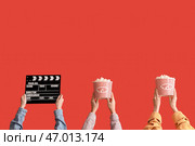 Множество рук с ведрами попкорна и киношным хлопушкой на красном фоне. Стоковое фото, фотограф Pixel_shot / Фотобанк Лори