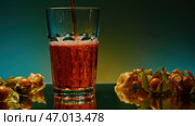 A green-lit background with a transparent glass around tangerines into which a cocktail is poured. Стоковое фото, фотограф David Kashakhi / Фотобанк Лори