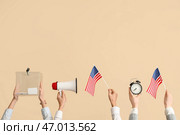 Руки с избирательной урной, флаги США, мегафон и будильник на бежевом фоне. Концепция выборов. Стоковое фото, фотограф Pixel_shot / Фотобанк Лори