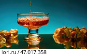 Golden whiskey pouring in the glass standing on glass reflective surface. Стоковое фото, фотограф David Kashakhi / Фотобанк Лори