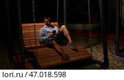 Man lying on wooden bench and swinging slowly, looking thoughtful. Стоковое фото, фотограф David Kashakhi / Фотобанк Лори