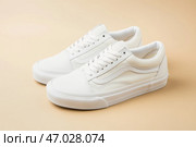 White leather lace-up running shoes with low tops, thick soles on a beige. The laces and rubber outsole. Sporty look. Men to wear during outdoor activities. Street hiking shoes. Trendy Male Boots Pair. Стоковое AI-изображение, AI-художник Марина Демидюк / Фотобанк Лори