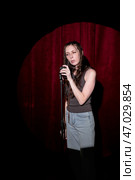 Young woman in jeans and a T-shirt standing behind a microphone on stage and singing. Performing a monologue on stage. Стоковое фото, фотограф Кашапова Эльвира / Фотобанк Лори