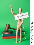 Деревянный манекен держит бумагу со словом IMPEACHMENT, книги и судейский молоток на цветном фоне. Стоковое фото, фотограф Pixel_shot / Фотобанк Лори