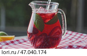 A pitcher of refreshing strawberry iced tea with mint leaves and ice cubes, set on a red and white checkered tablecloth, with slices of fruit in the background. Стоковое AI-видео, аниматор Башкирова Анна / Фотобанк Лори
