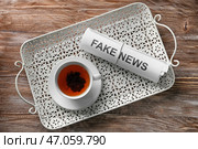 Рулон бумаг с фразой «Фальшивые новости» и чашкой чая на деревянном столе. Стоковое фото, фотограф Pixel_shot / Фотобанк Лори