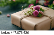 Beautifully wrapped gift in biodegradable paper adorned with fresh flowers. Красиво упакованный подарок в биоразлагаемую бумагу, украшенный живыми цветами. Стоковое AI-изображение, AI-художник Katsiaryna Repich / Фотобанк Лори