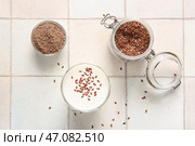 Стакан свежего йогурта с льняными семенами и миска с мукой на белом кафельном фоне. Стоковое фото, фотограф Pixel_shot / Фотобанк Лори